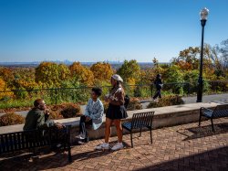 Three students sitting outside and chatting with New York City skyline in the background.