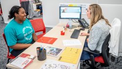 University College employee meeting with smiling student at office desk.