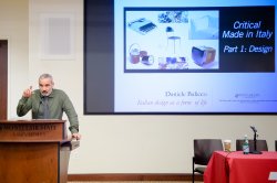 Image of a speaker presenting in front of a projection.
