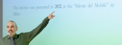 Photo of a speaker presenting in front of a screen and pointing.