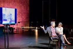 Image of two people sitting and presenting on stage with a screen behind them with a piece of artwork depicted.