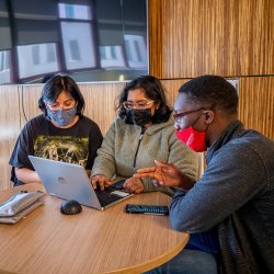 A group of students sit together at a table, looking at a laptop.