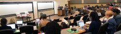 Wide photograph encompassing a large faculty audience seated in a lecture hall.