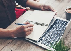 Young business man hand writing notebook and using laptop on a table