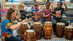 Children beating drums with instructor