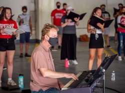 instructor on piano backed by choir students