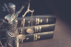 Image of law books in the background with a small scales of justice statue in the foreground.