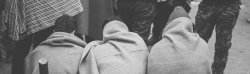black and white photo. Three people are wrapped in blankets, their backs to the camera