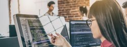 Image of worker pointing to a computer screen with code on it in a team setting.