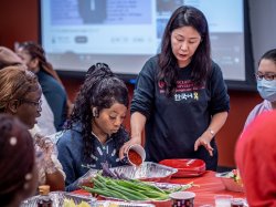 Woman pours spices into a dish while others look on
