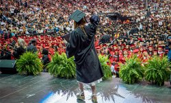 photo of student at graduation crossing stage with the whole crowd in background