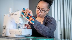 Awilda Quezada Puntiel removing mask from sewing machine