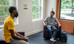 two students sit apart with face masks on in the residence life office