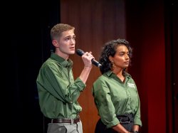 Two green teams members on stage, one speaking into microphone