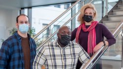 Three students wearing masks posing on a staircase