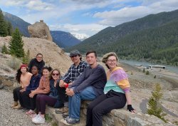 students seated on low rock wall, scenic valley view beyond