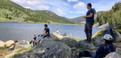 students sitting on rocks along the bank of a reservoir