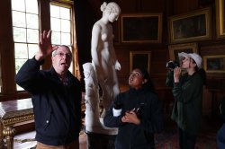 two people speaking in foreground, sculpture in background
