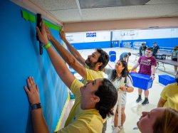 President Koppell placing trim on a bulletin board with students