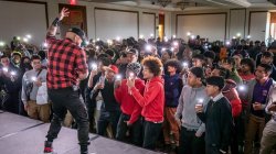 A crowd of students direct their lighted phones at a man on stage.