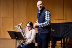 Female student with an instrument that looks like a small tuba with male professor.