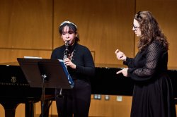 Female student plays clarinet for female teacher.
