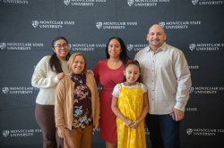 A family gathers in front of a banner for a photo.