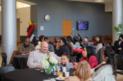 People of various ages and ethnicities sit at tables at an event.