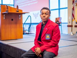 A young man sits on a stage and poses for a photograph.