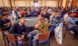 Many young men and a few women sit at tables in a conference room.