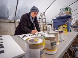Female paints lettering on a sign.