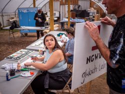 Female student looks at man holding sign. Two other students paint at tables.