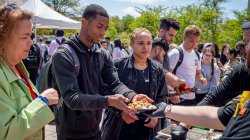 A male student takes a plate from a food vendor as others look on.