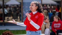 A female student smiles as she speaks into a microphone on a sunny day.