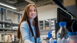 A female student smiles at a computer in a science lab.