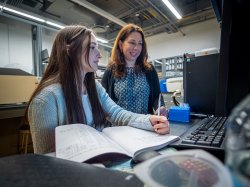 A student and a professor look at a computer screen in a science lab.