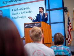 President Koppell gestures and speaks to an audience from podium on stage