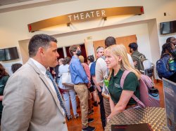 A man and woman talk to each other in front of a theater entrance with other people in the background.