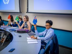 Four students hold flags of different countries while sitting at a curved table.