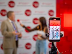 A closeup of a cell phone shows the video of a student interviewing a man.