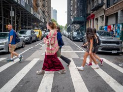 Five people walk on over the striped lines of a NYC crosswalk.