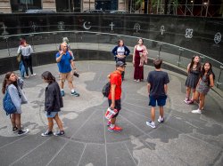 Group of nine students and a professor stand on a circular map of earth.