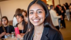 A high school student smiles in a conference room filled with other students.