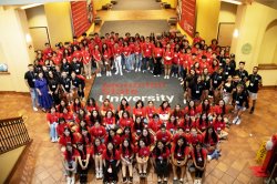 A large group of students, mostly in red t-shirts, encircle a Montclair State University sign.