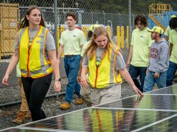 Students wearing yellow safety vests tour a facility.