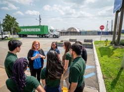 A woman talks with a group of students in a parking lot.