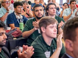 Several male students in an audience applaud.