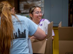 A young woman smiles as she packs a box of supplies.