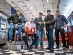 Five men from rock bands pose in a retro diner.