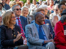 A man and a woman smile with a crowd of smiling people behind them.